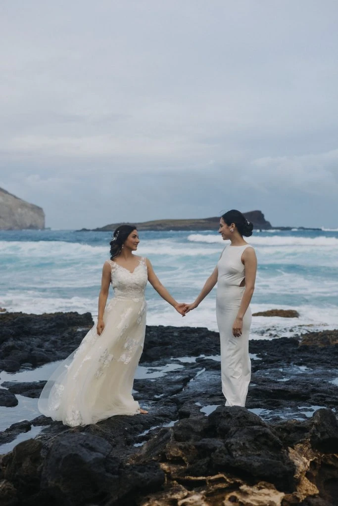 Two brides holding hands on a rocky beach