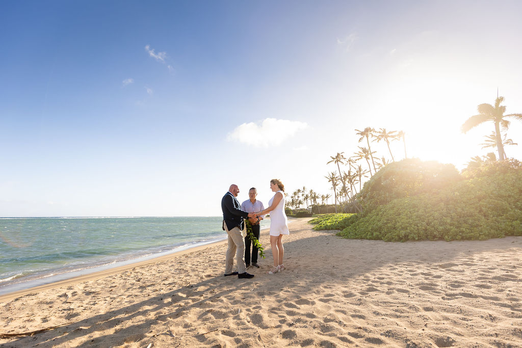 Rev. James Chun officiating a destination wedding on an Oahu beach at sunset.