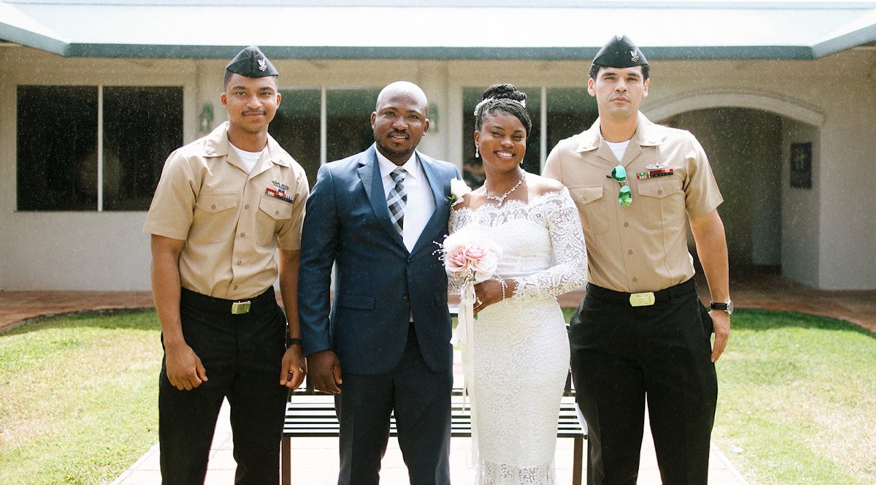 A newly married military couple smiling with two U.S. Navy service members in uniform outside a Honolulu wedding venue on Oahu.