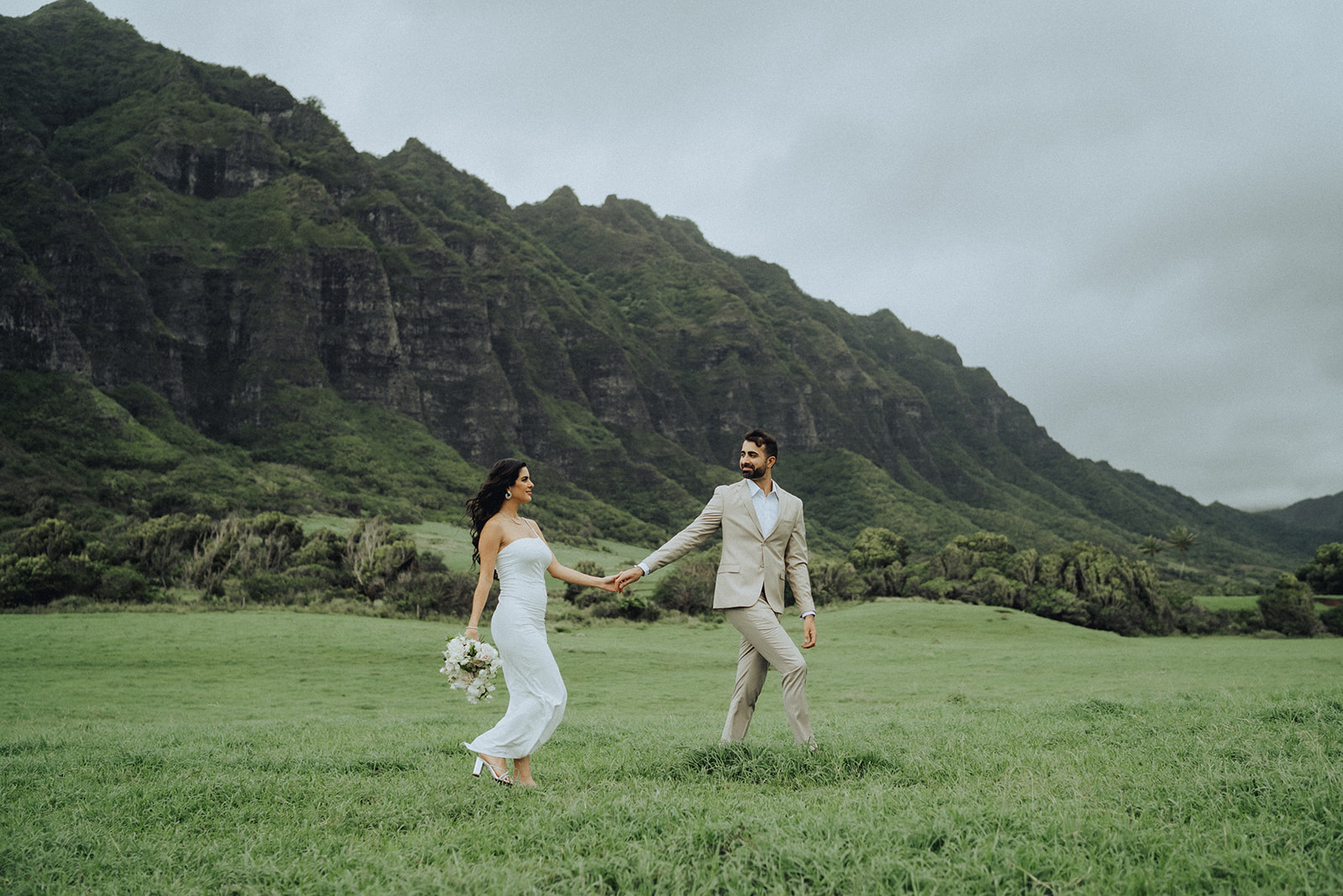 Scenic landscape view of a beach wedding at Kualoa Regional Park on Oahu with dramatic green mountain cliffs in the background