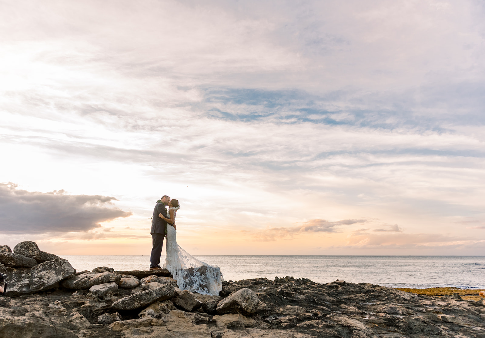 Bride and groom kissing on coastal rocks at Ko Olina during sunset, one of the best sunset wedding locations on Oahu.