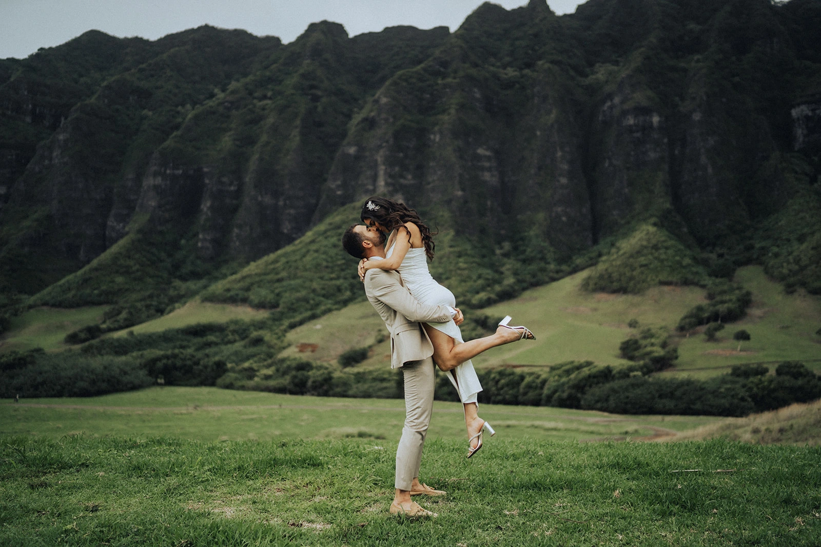 Groom lifting bride in a passionate embrace during Kualoa Regional Park weddings framed by the emerald Koʻolau mountain peaks